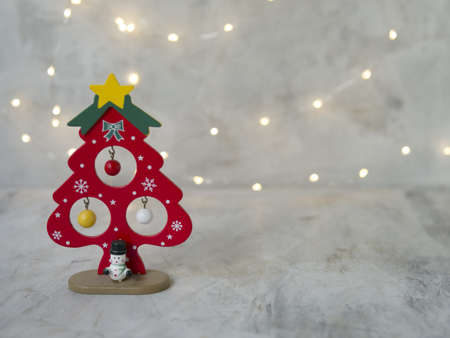 a wooden Christmas red tree with yellow star, small colored balls and snowman on a gray background of glowing lights. New Year card. Christmas concept. Selective focus, place for textの写真素材