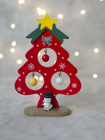 a wooden Christmas red tree with yellow star, small colored balls and snowman on a gray background of glowing lights. New Year card. Christmas concept. Selective focus, place for textの写真素材