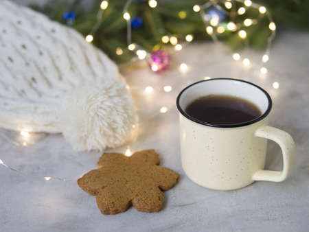 Christmas background with Gingerbread cookies, cup of tea. Cozy evening, Christmas decorations, colored balls and lights garlands, white knitted hat. New Year card. Place for text, selective focusの写真素材