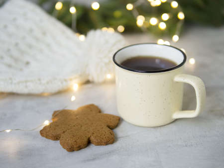 Christmas background with Gingerbread cookies, cup of tea. Cozy evening, mug of drink, Christmas decorations, lights garlands, white knitted hat. New Year card. Copy space, selective focusの写真素材