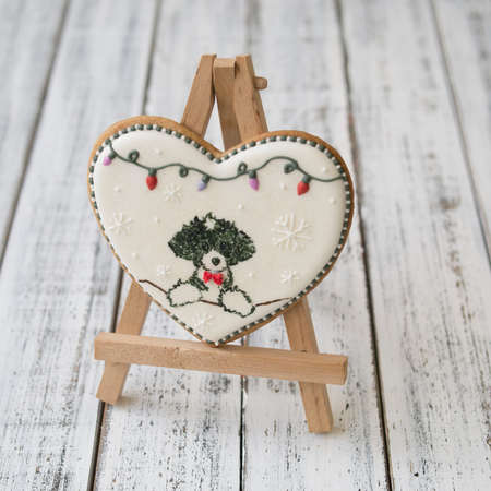 A glaze Christmas gingerbread cookie in the shape of a heart with a cute puppy and New Years garland on a white wooden table. Close up, selective focus, copy space, flat lay, top viewの写真素材