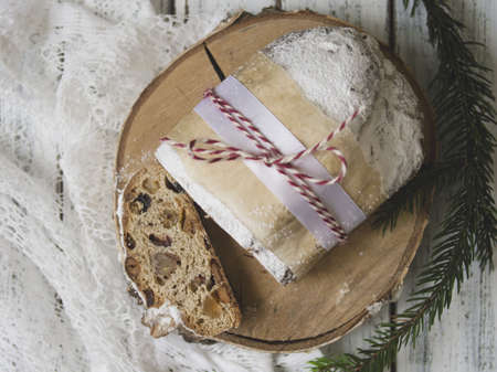 Traditional Christmas festive pastry dessert with festive decoration - spruce twigs and tangerines. Slice of Christmas stollen on white wooden background. Top view, copy spaceの写真素材