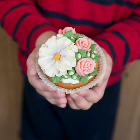 Homemade sponge cupcakes with flowers buttercream frosting. The boy is holding decorated cupcake. Sweet gift to mom,teacher or girlfriend for March 8, Valentine's Day or Teacher's Day.Selective focusの写真素材
