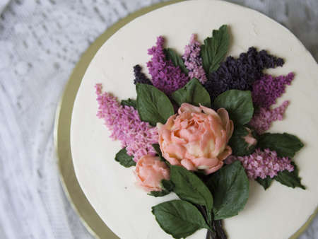 White cake decorated with buttercream flowers - lilac, peonies - on wooden background with lace fabric. Vintage, retro. Gift for Women's Day, 8 March, Valentine's Day. Close up, copy space, top viewの写真素材