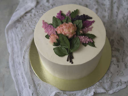 White cream cake decorated with buttercream flowers - lilac, peonies - on wooden background with lace fabric. Vintage, retro. Gift for Women's Day, 8 March, Vaentine's Day. Close up, copy spaceの写真素材