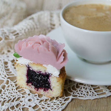Cupcakes decorated with cream flowers rose on wooden background with a lacy napkin with cup of coffee. Piece of cupcake. Breakfast on Valentine's Day.Gift for Women's Day.Selective focus, copy spaceの写真素材