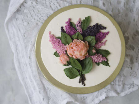 White cake decorated with buttercream flowers - lilac, peonies - on wooden background with lace fabric. Vintage, retro. Gift for Women's Day, 8 March, Valentine's Day. Close up, copy space, top viewの写真素材
