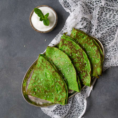 Green mint crepes with Sour Cream and Mint Leaf on metal plate on gray background with lace fabric. Close up, copy space, top view, selective focus, squareの写真素材