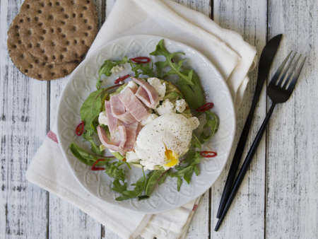 Healthy breakfast, sweet potatoes, cheese, avocado, ham, poached egg and greens with whole grain bread. Diet food. Breakfast served on a white plate on a light wooden table. Close up. Top view.の写真素材