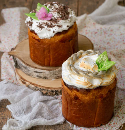 Easter composition with orthodox sweet bread, kulich decorated with flowers and leaves of marzipan on wooden background with floral fabric. Easter holidays. Selective focus, close up, copy spaceの写真素材