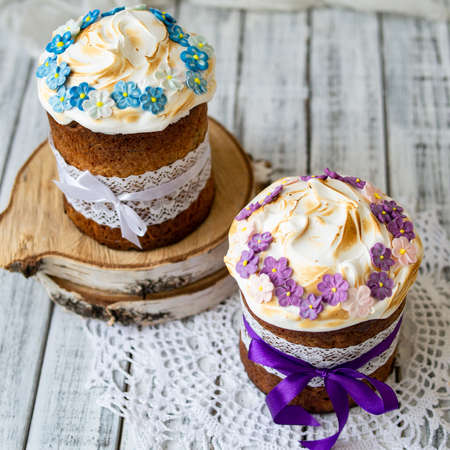 Two traditionally baked orthodox paskas with glace icing and bright blue and violet flowers on white...