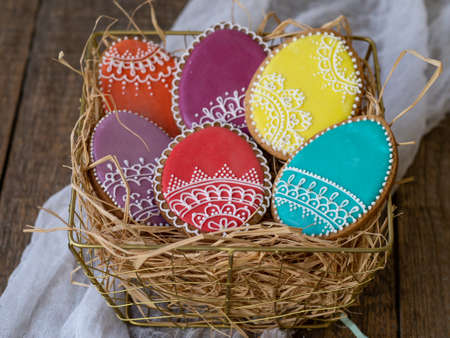 Colored cookies in the form of Easter beautiful eggs with icing lace in a metal golden basket with...