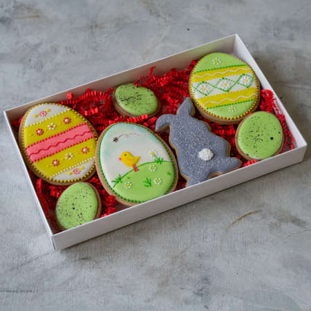 Happy family holiday, presents in box , gingerbread easter cookies in form of rabbits and eggs. Festive cookies in white box on gray background. Selective focus, close up, copy spaceの写真素材