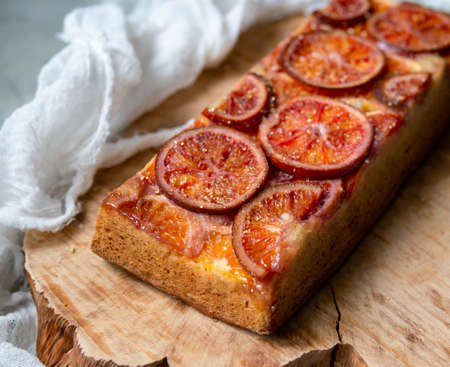 Homemade cake with blood oranges on on a wooden board and light gray background. Slice of cake. Piece of pie. Scandinavian style. Selective focus, copy space, close upの写真素材