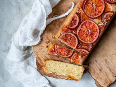 Homemade cake with blood oranges on on a wooden board and light gray background. Slice of cake. Piece of pie. Scandinavian style. Selective focus, copy space, close upの写真素材