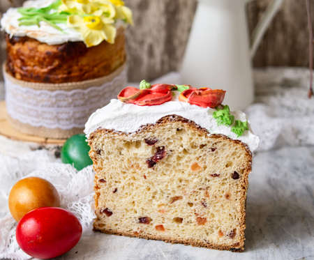 Easter cake kulich.Traditional sweet bread decorated meringue, yellow daffodils on gray background with lace fabric and colored eggs. Copy space, selective focus.Slice of cake.season's greetings card.の写真素材