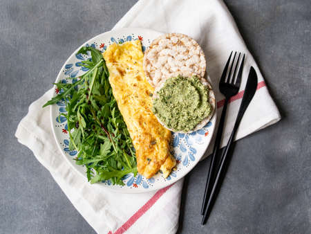 Healthy breakfast - scrambled eggs, arugula and bread with pesto on gray background. Perfect eggs omelette with fresh arugula and pesto cracker. Vegetarian food. Diet. Selective focus, close upの写真素材