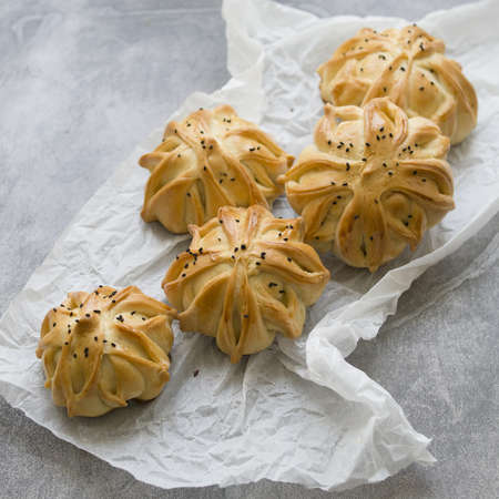 Interestingly shaped fresh meat mini pie on the gray table with white paper. Meat pies samosas with ground beef and spices. Menu, recipe concept. Selective focus. Closeup, top view, rustic styleの写真素材