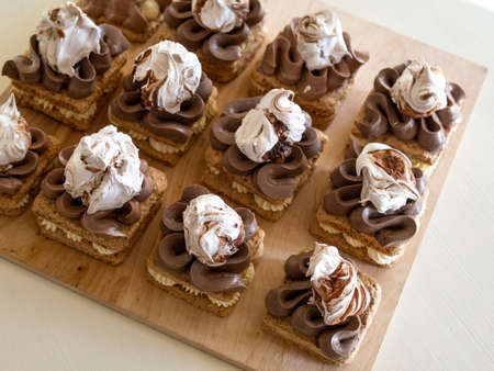 Portion cakes of meringue and cocoa butter cream in square form on a wooden stand, a piece of cake on a light wooden background. Restaurant serving. Selective focus, close upの写真素材