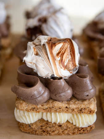 Portion cakes of meringue and cocoa butter cream in square form on a wooden stand, a piece of cake on a light wooden background. Restaurant serving. Selective focus, close upの写真素材