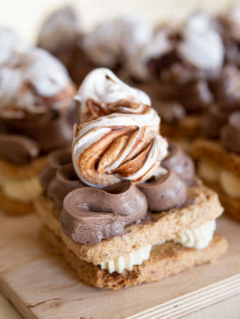 Portion cakes of meringue and cocoa butter cream in square form on a wooden stand, a piece of cake on a light wooden background. Restaurant serving. Selective focus, close upの写真素材