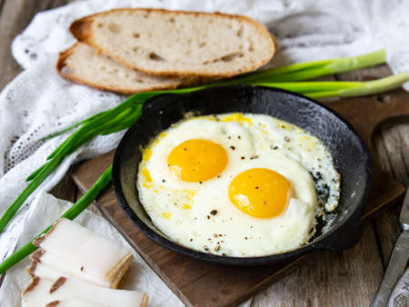 Scrambled eggs in frying pan with pork lard, bread and green feathers onions on old wooden table. National Ukrainian or belorussian food. Breakfast, lunch. Close up, selective focus, rustic style.の写真素材