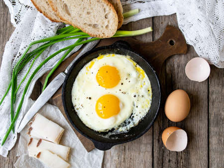 Scrambled eggs in frying pan with pork lard, bread and green feathers onions on old wooden table. National Ukrainian or belorussian food. Breakfast, lunch. Top view, selective focus, rustic style.の写真素材