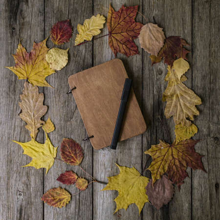 Autumn composition with workspace with blank notebook, pencil and beautiful colored dry leaves. Top view, flat lay, vintage toning. Autumn relax concept.の写真素材
