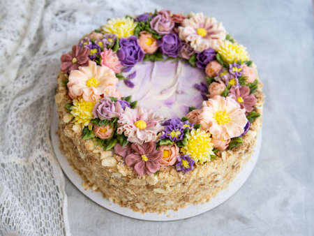 Napoleon cake with vanilla cream, decorated with buttercream flowers - roses, scabioses, chrysanthemums in pink, yellow, purple colors. Vintage style. Gray background, lace napkin.Copy space, close upの写真素材