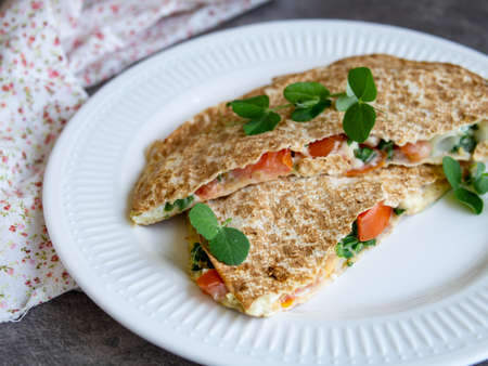 Vegetarian healthy breakfast of melted thin pita bread, cheese, tomato and herbs on a white plate and gray background. Diet. Selective focus, close up, copy spaceの写真素材