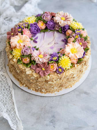 Napoleon cake with vanilla cream, decorated with buttercream flowers - roses, scabioses, chrysanthemums in pink, yellow, purple colors. Vintage style. Gray background, lace napkin.Copy space, close upの写真素材