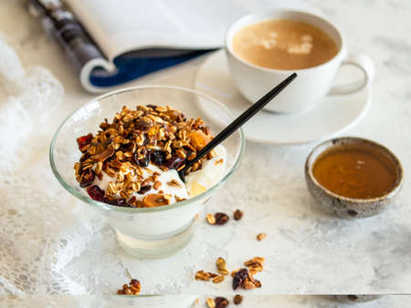 Healthy breakfast. Granola, muesli with pumpkin seeds, honey, yogurt in a glass bowl with a cup of coffee on white background. Breakfast of a modern girl. Close up, copy space.の写真素材