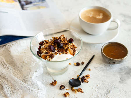 Healthy breakfast. Granola, muesli with pumpkin seeds, honey, yogurt in a glass bowl with a cup of coffee on white background. Breakfast of a modern girl. Close up, copy space.の写真素材