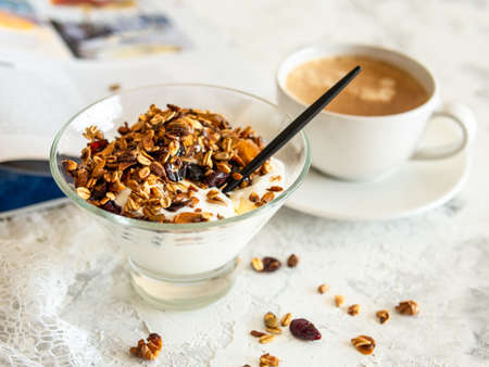 Healthy breakfast. Granola, muesli with pumpkin seeds, honey, yogurt in a glass bowl with a cup of coffee on white background. Breakfast of a modern girl. Close up, copy space.の写真素材