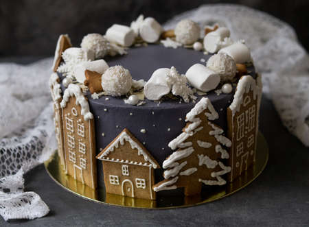 Christmas gray cake decoraited of gingerbread cookies in shape of homes and snowy christmas trees, marshmallows, snowflakes, sweets. Christmas, New Year greeting card. Gray background. Copy space.の写真素材