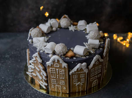 Christmas gray cake decoraited of gingerbread cookies in shape of homes and snowy trees, marshmallows, snowflakes, sweets. Christmas, New Year greeting card. Gray background with garland. Copy space.の写真素材