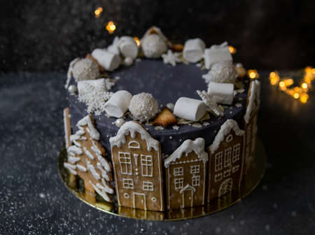 Christmas gray cake decoraited of gingerbread cookies in shape of homes and snowy trees, marshmallows, snowflakes, sweets. Christmas, New Year greeting card. Gray background with garland. Copy space.の写真素材
