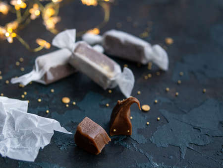 Fresh gold caramel toffee candies in white paper on blue dark background with garland in the form of luminous stars. Christmas,New Year greeting card. Close up, copy space. Top viewの写真素材