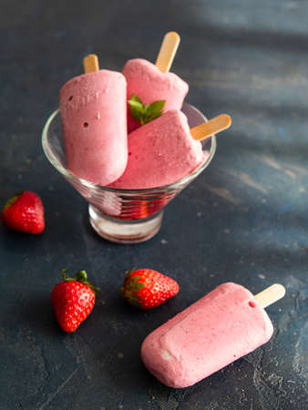 Strawberry ice cream on a stick of yogurt in a glass bowl on a dark background. Diet, healthy eating. Close up, copy space. Good food for hot weather, summer.の写真素材