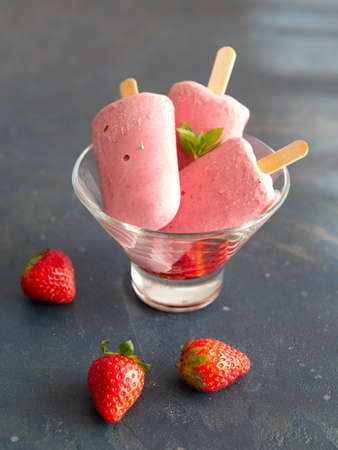 Strawberry ice cream on a stick of yogurt in a glass bowl on a dark background. Diet, healthy eating. Close up, copy space. Good food for hot weather, summer.の写真素材