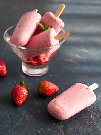 Strawberry ice cream on a stick of yogurt in a glass bowl on a dark background. Diet, healthy eating. Close up, copy space. Good food for hot weather, summer.の写真素材
