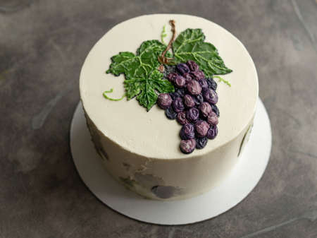 White birthday cake with painted blue grapes on grey background. Buttercream. Close up, copy space. top view.の写真素材