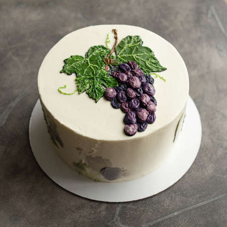White birthday cake with painted blue grapes on grey background. Buttercream. Close up, copy space. top view.の写真素材