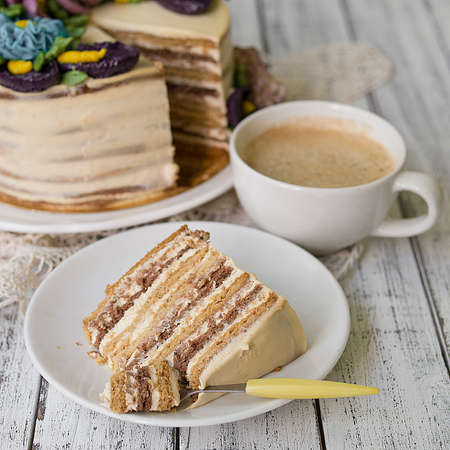 Honey cake on a white table with cup of coffe. Cake with cream flowers. Close up, copy space.の写真素材