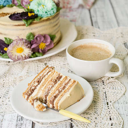 Honey cake on a white table with cup of coffe. Cake with cream flowers. Close up, copy space.の写真素材