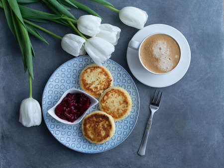 Syrniki, curd or cottage cheese pancakes with cherry jam and coffee on a grey background With white tulips, top view. Healthy diet breakfastの写真素材