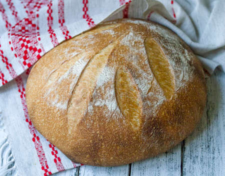 Traditional wheat freshly rustic baked bread with whole grain flour on white wooden background with national linen. Artisan sourdough bread. Close up.の写真素材