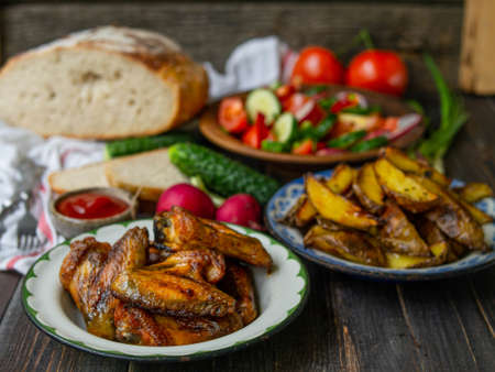 French fries, wings, salad, vegetables, bread on an old wooden background. Rural dinner, summer picnic. Top view. Flat lay.の写真素材