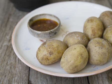 Boiled potatoes in their skins. whole with red pepper, salt and spicy sauce on white plate, old wooden table, rustic style. Close up, copy space.の写真素材