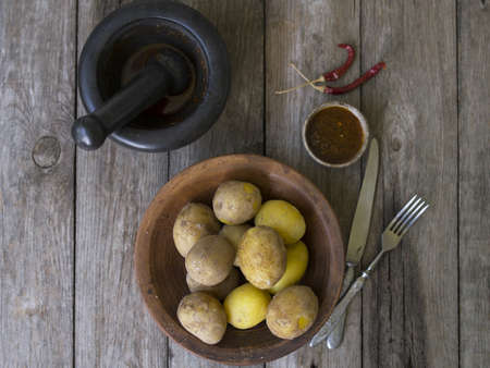 Boiled potatoes in their skins. whole with red pepper, salt and spicy sauce on clay plate, old wooden table, rustic style. Close up, copy space. Top view.の写真素材